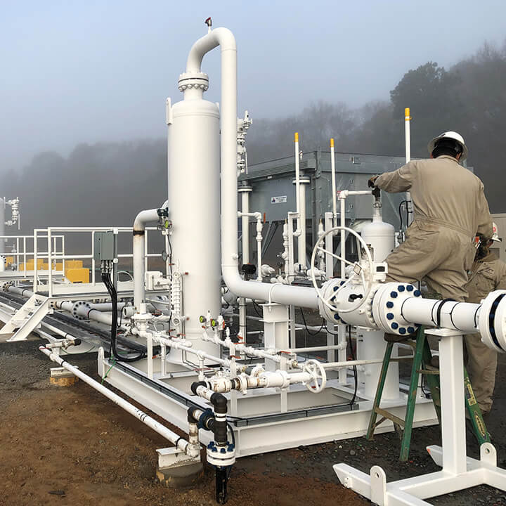 Worker adjusting valves on newly installed white piping at an industrial gas processing plant