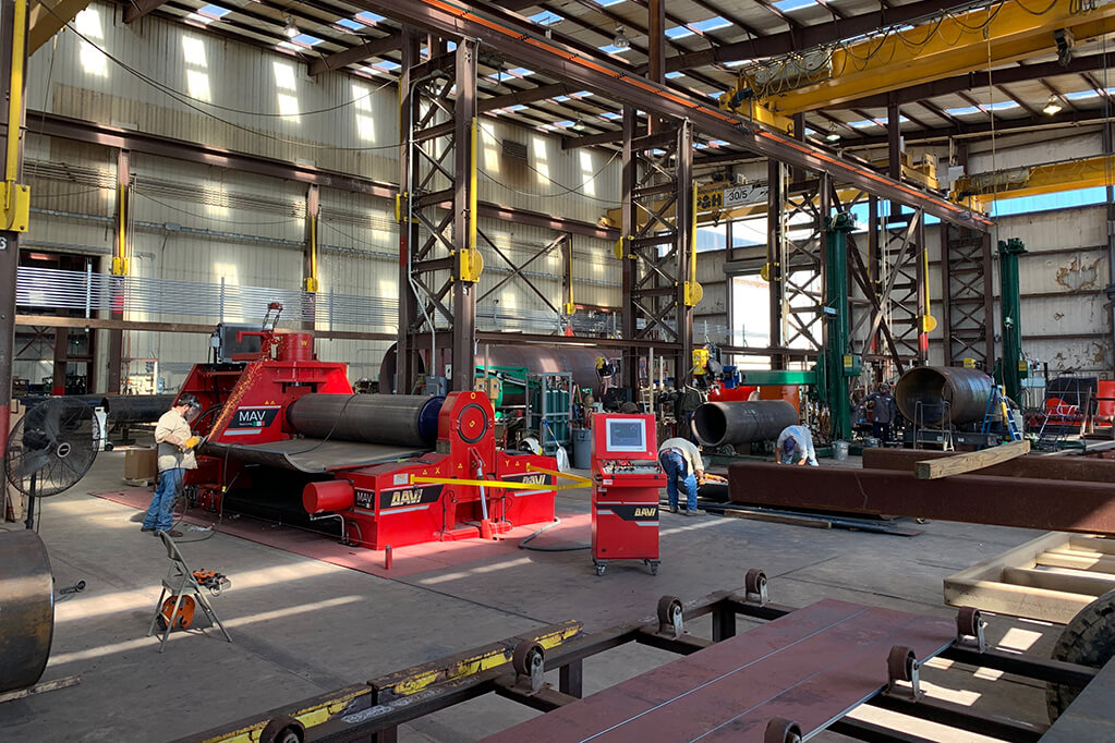Busy industrial workshop with heavy machinery and a worker welding