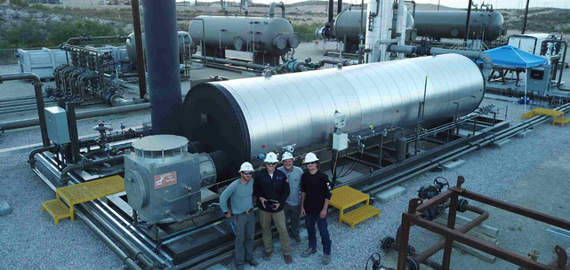 Four workers in hard hats standing in front of industrial equipment at a gas processing facility