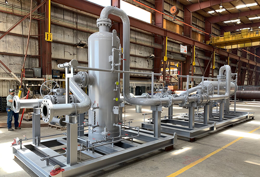 Industrial piping module with tanks and valves inside a manufacturing facility, with a worker present.